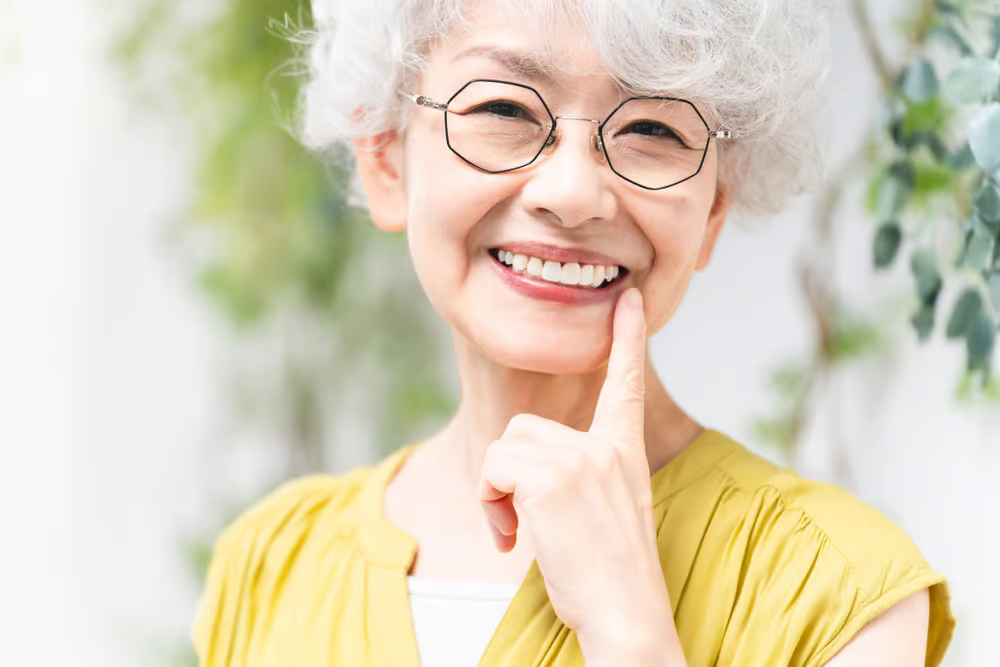 Senior woman with glasses smiling confidently after dental implants - การทำรากฟันเทียมในผู้สูงอายุโดยทันตแพทย์เฉพาะทาง Global Dental Complex
